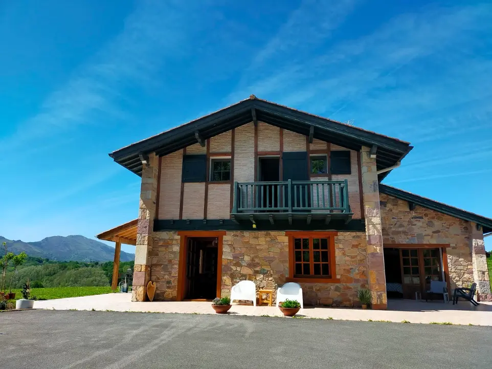 Maison d'hôtes GOITIK IKUSITA avec façade en pierre et bois, nichée dans le Pays Basque, offrant une vue sur les montagnes des Pyrénées