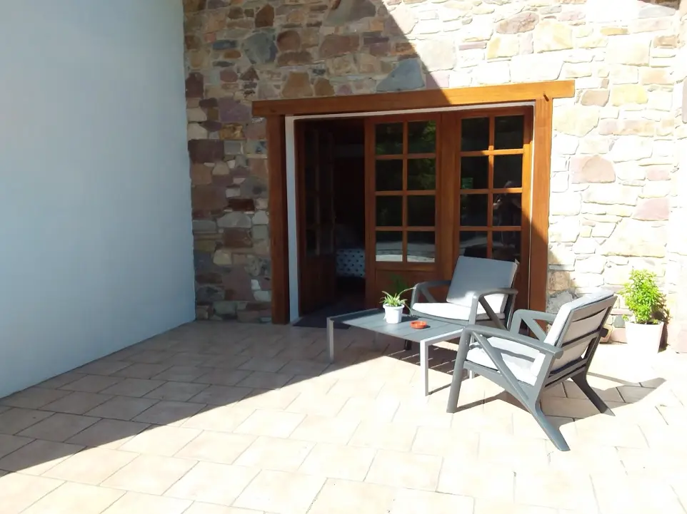 Terrasse accueillante de la maison d'hôtes GOITIK IKUSITA avec mobilier de jardin moderne et porte-fenêtre en bois ouvrant sur l'intérieur cosy.