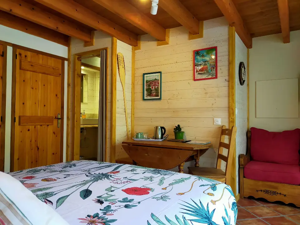 Chambre confortable avec des éléments en bois, un canapé rouge, une télévision murale et une table pliante dans le gîte Goitik Ikusita à Ainhoa.