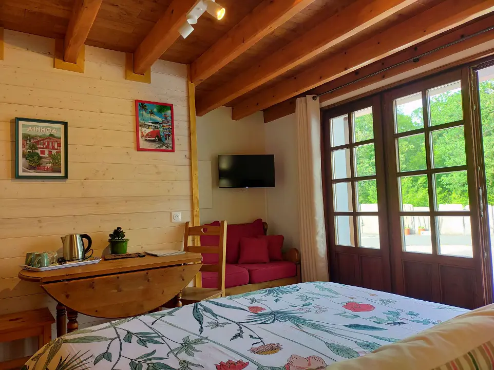 Chambre confortable avec des éléments en bois, un canapé rouge, une télévision murale et une table pliante dans le gîte Goitik Ikusita à Ainhoa.